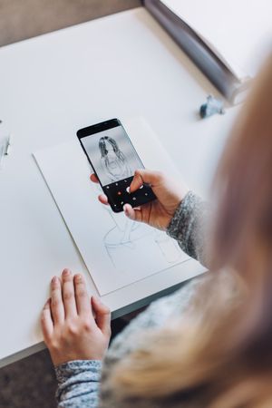 Woman with smartphone taking photo of paper with sketch