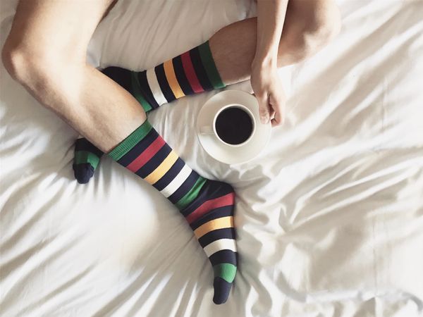 Person in a colorful socks holding a cup of coffee and sitting on a bed
