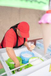 An Hispanic adult woman is serving some ice cream in plastic cups in the street