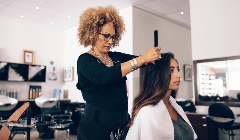 Focused hairdresser preparing female client hair for trim