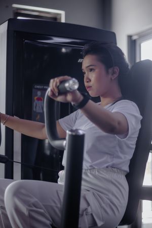 Dedicated young woman using chest press machine at modern fitnes
