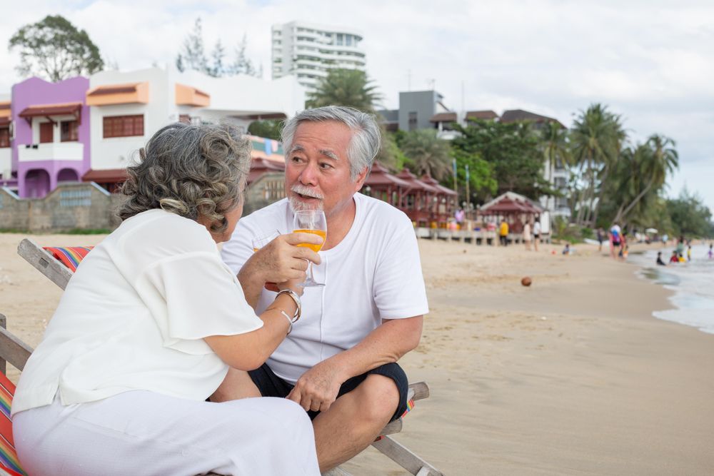Older Asian couple relaxing on the beach with drinks