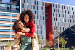 Smiling female friends piggy backing outside on sunny day