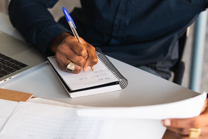 Black man writing in notepad near laptop in office