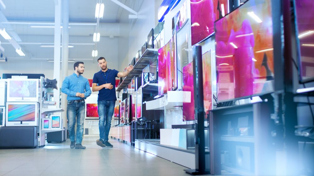In the Electronics Store Professional Consultant Shows Latest 4K TV's to a Man, They Talk about Specifications and What Model is Best for Young Man's Home.