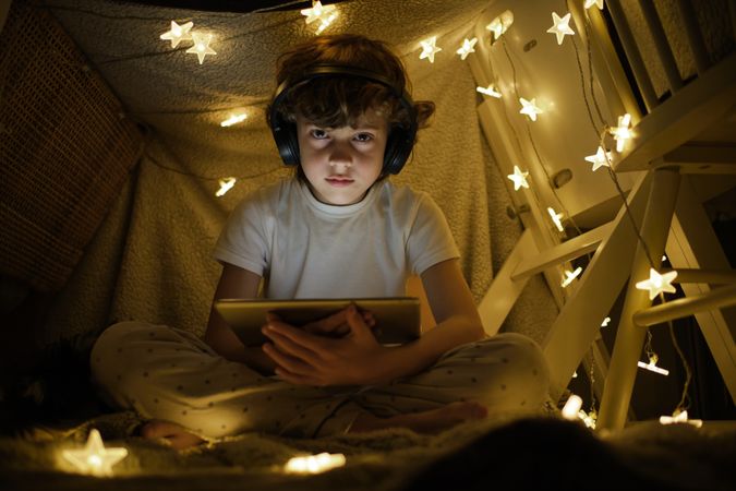 Serious boy using tablet and headphones in tent