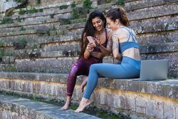 Smiling multiethnic women using smartphone after yoga practice