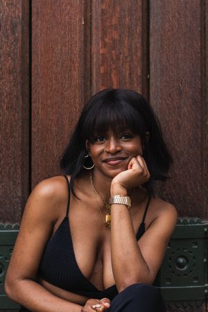 Cheerful Black woman in black outfit against wooden wall