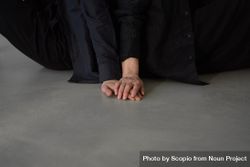 Cropped image of two people in dark outfit touching hands on floor bGXme0