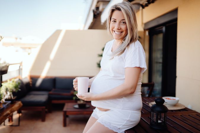 Smiling pregnant woman having drink at terrace
