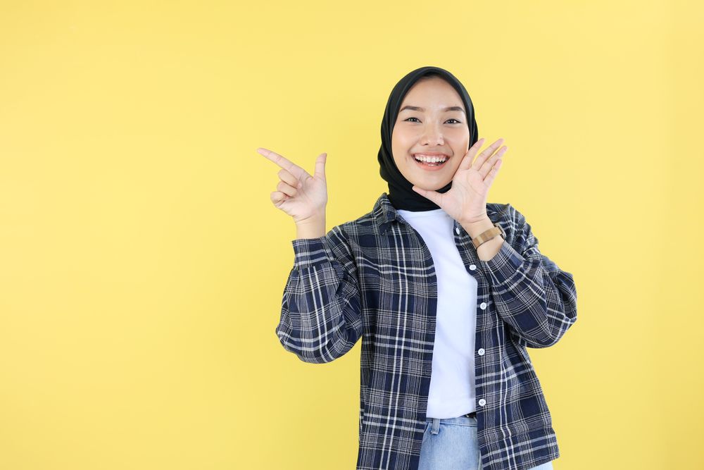 Happy Indonesian Young Woman in Veil or Hijab, Pointing at Copy Space with Right Hand