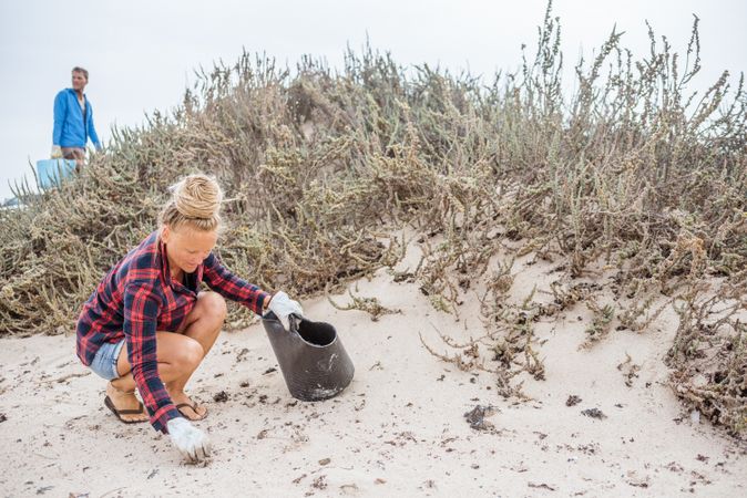Content modern woman picking litter from sandy seashore