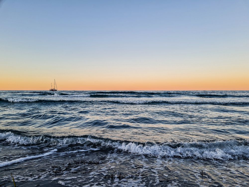 Ocean waves crashing on shore during sunset with boat in the horizon