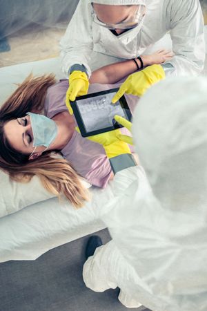 Top view of doctors in protective suit examining x-ray of patient on tablet