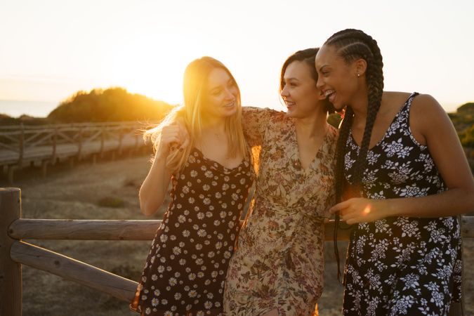 Women in summer dresses hanging out together leaning on wooden fence on coast at magic hour