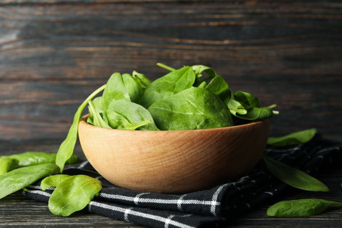Wooden bowl with spinach and napkin on wooden background