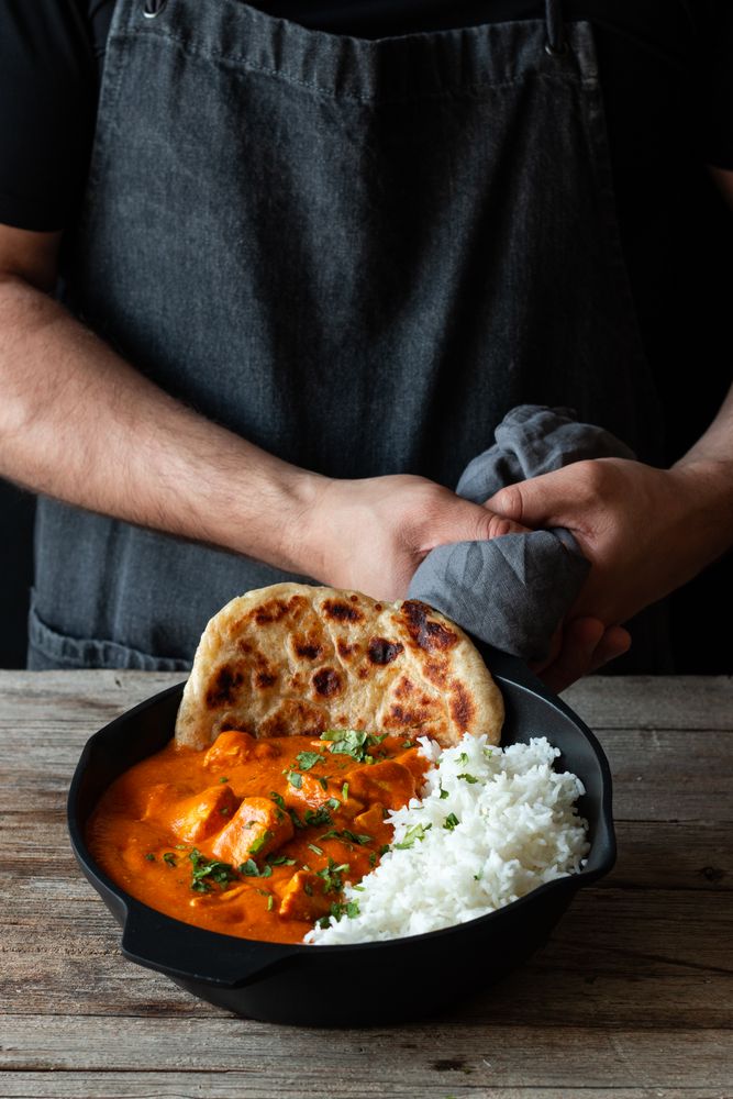 Faceless cook holding frying pan with hot butter chicken
