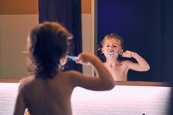 Funny boy brushing teeth with brush in bathroom