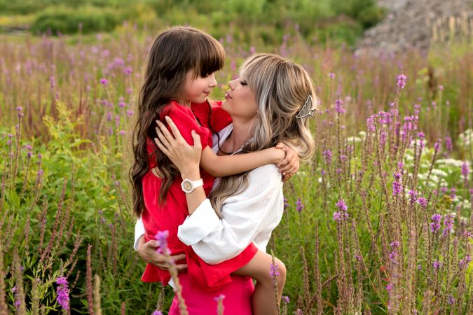 Mom and little daughter walking among meadow flowers
