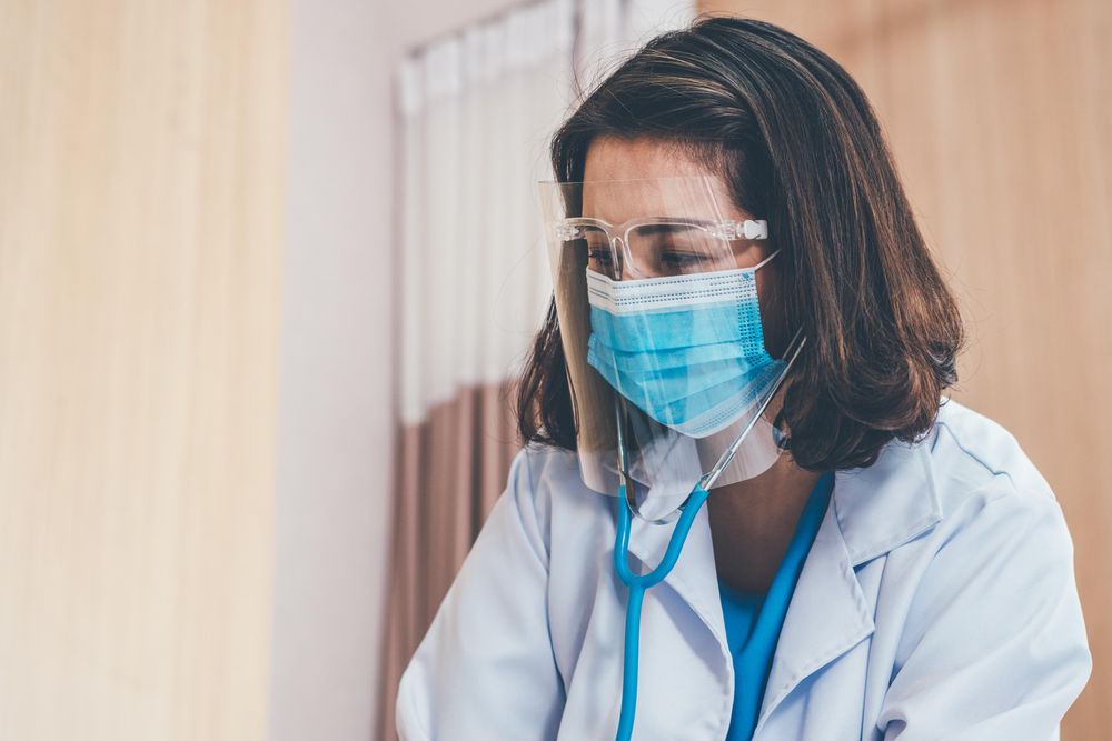 Female doctor in facemask and shield wearing stethoscope in hospital setting