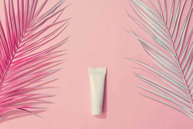 Painted leaves and sunscreen on pastel pink background