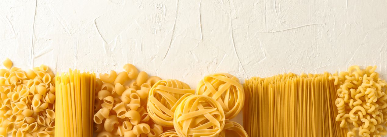 Different pasta on light background, space for text. Dry uncooked whole pasta