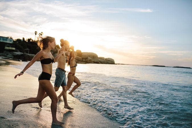 Group of happy friends running to the sea on sunset
