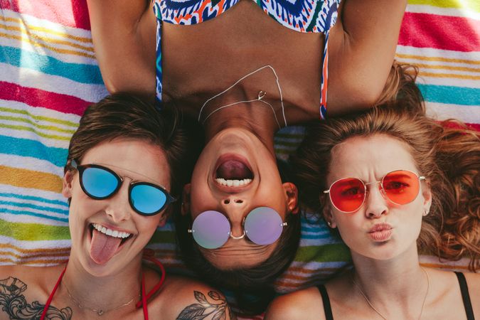 Top view of happy friends lying on a towel at the beach wearing colorful sunglasses