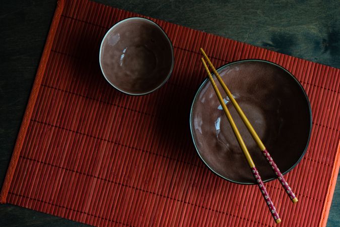 Two bowls with chopsticks on red table mat