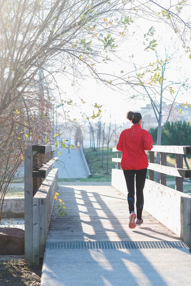 Back of woman running outdoors in a city park on sunny day