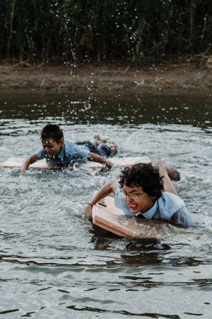 Happy boys swimming with board over water