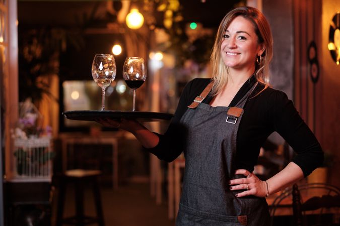 Cheerful waitress holding tray with wineglasses