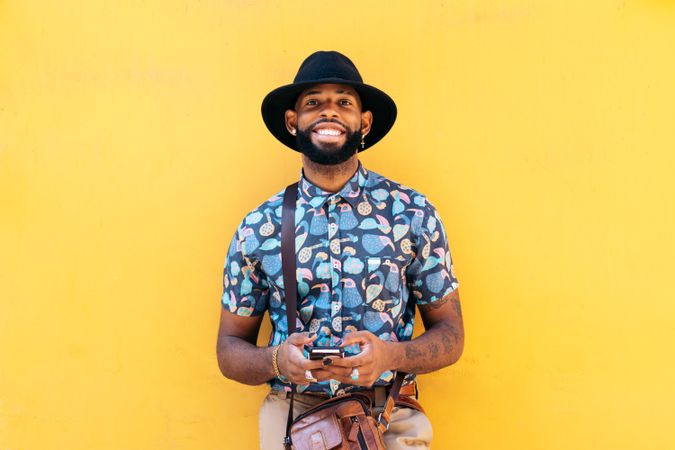 Stylish Black man using smartphone outdoors over yellow background