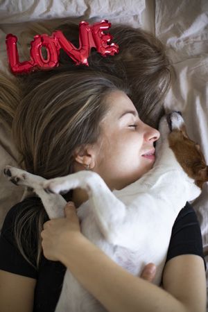 Woman lying on the bed holding her dog and a red love balloon above her head