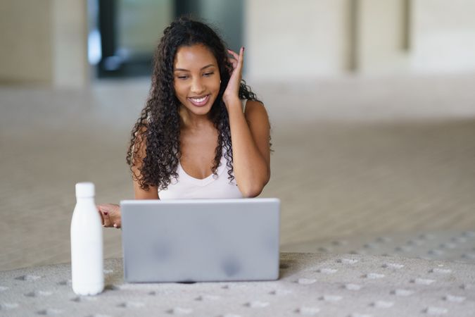 A young woman is happily engaged online with her laptop and enjoying a refreshing water