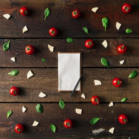 Basil, tomatoes, and cheese on wooden background with notepad