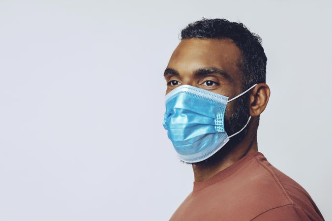 Sideview of male looking at camera wearing medical face mask in studio shoot, copy space