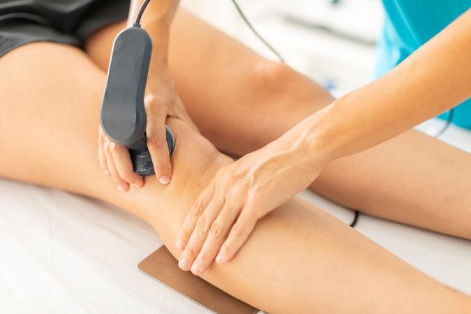 A physical therapist applies radiofrequency waves with a diathermy machine to relieve her patient's knee muscle pain