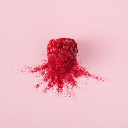 Single raspberry with red dust on pink background