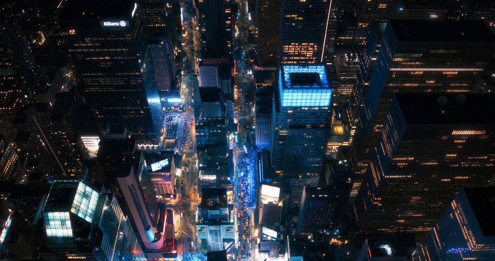 Night Aerial Image of New York City with Skyscraper Spires and Straight Busy Streets with Cars and Yellow Taxi Vehicles. Top Down Helicopter View of Office Buildings in a Big Urban Center