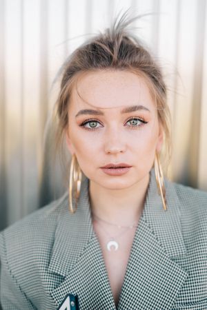 Woman with tablet in stylish suit standing nearby wall holding sunglasses