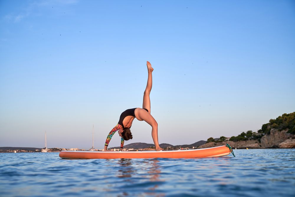 Flexible woman practicing yoga on paddleboard
