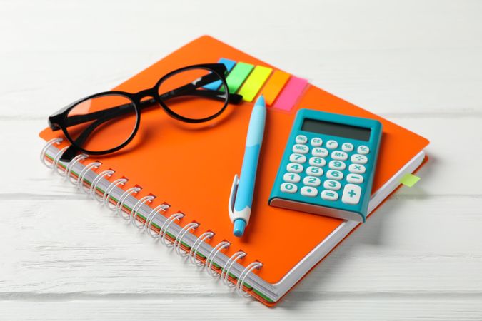 Orange notebook with glasses and stationary on table