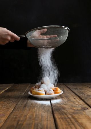 Person sprinkling icing sugar over on cookies