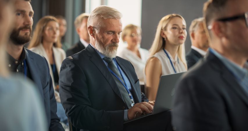 Male Top Manager Sitting In Crowd And Using Laptop Computer At International Technology Conference.