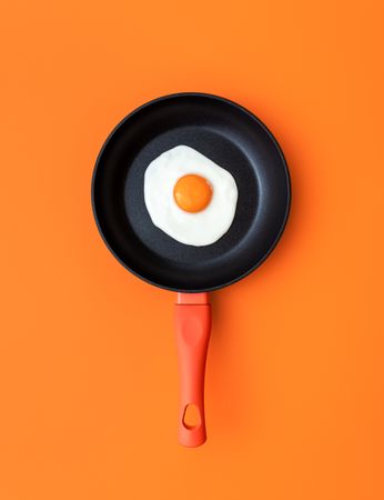 Fried egg in a cooking pan, top view on an orange background