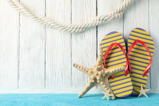 Flip flops and starfishes on wooden background, space for text