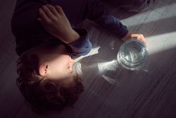 Calm boy in sunbeam glowing through jar with water