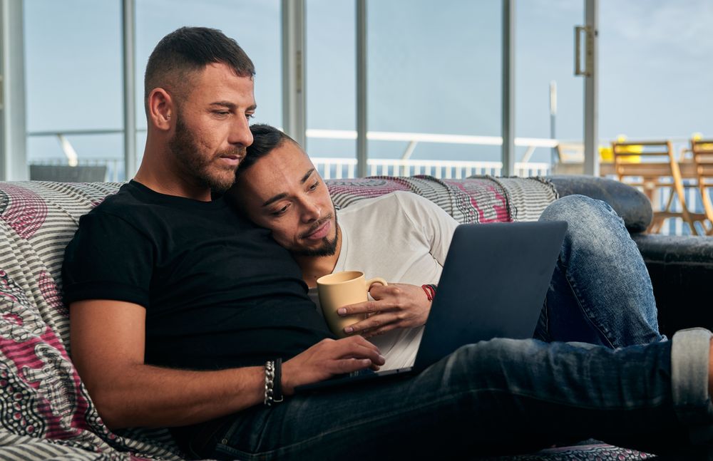 Happy gay couple using laptop at home