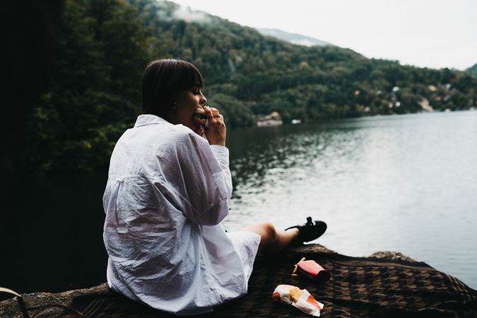 Woman eating hamburger near lake and mountains